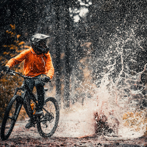 A mountain biker who has just splashed through a muddy puddle in a forest, looking off to the side.