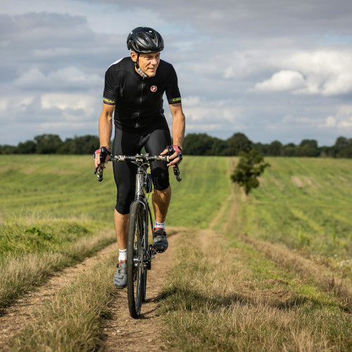 A male cyclist riding towards the camera in a grassy field, looking off to the distance.