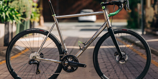 A Bossi Strada Classic titanium road bike, custom-built by Bio-Mechanics Cycles & Repairs, photographed in a sunny alleyway.