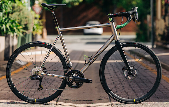 A Bossi Strada Classic titanium road bike, custom-built by Bio-Mechanics Cycles & Repairs, photographed in a sunny alleyway.