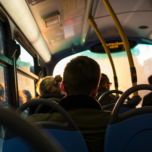 A man on a bus, seen from the point of view of someone sitting behind him.