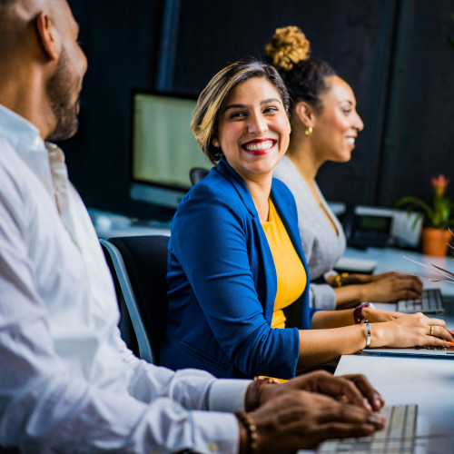 A row of office workers at keyboards, the woman in the middle smiling at the man sitting next to her.