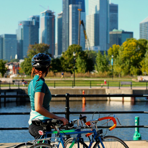 A woman in a bike helmet looks over towards a cityscape, two road bikes next to her.