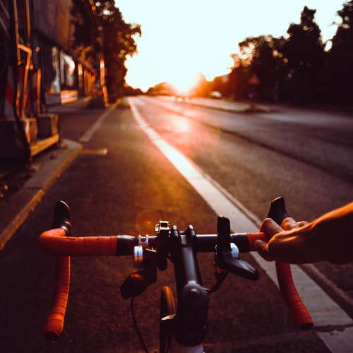 The view of a road from the point of view of a bike rider on a road bike. It's sunrise, and the road is empty.