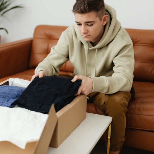 A young man unenthusiastically opens a gift of a box of clothes.