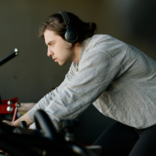A young man riding on a stationary bike, wearing headphones and looking serious.