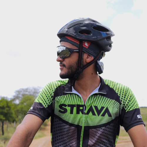 A male bike rider outside, wearing a green and black jersey with 'STRAVA' printed on the front.