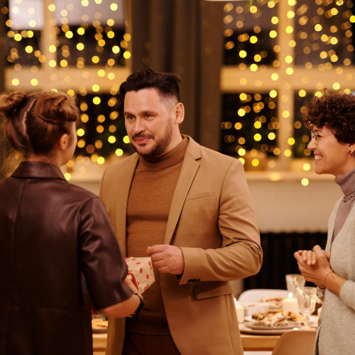 Two women present a man with a gift, looking excited.
