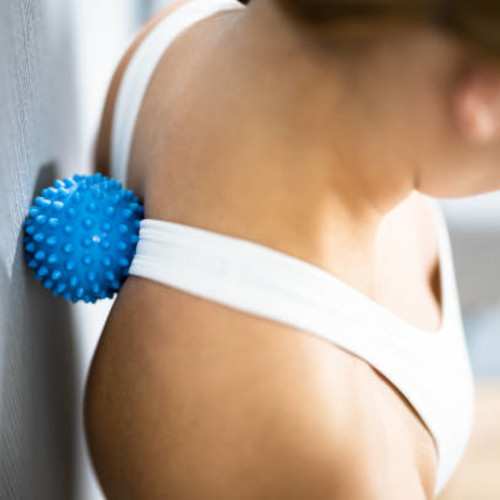 A person leaning against a wall, using a blue spiky trigger ball to release tension between their shoulder blades.