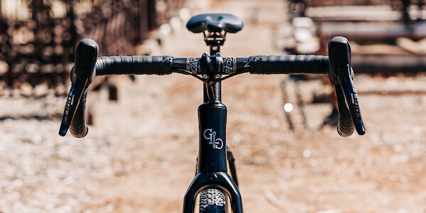 Front-on view of a Gothic Cycles Aix carbon gravel bicycle, created by Bio-Mechanics Cycles & Repairs, shot in a day-lit graveyard setting.