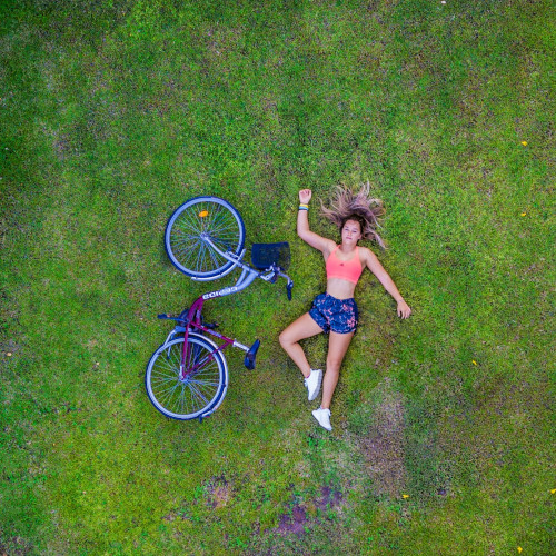 Overhead shot of a young woman lying on a lawn next to a bicycle.