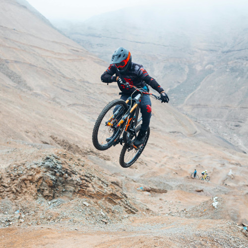 A mountain biker mid-air over a jump in an arid desert environment.