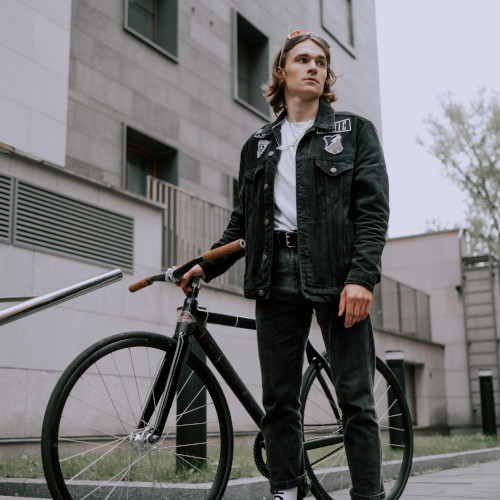 A young man stands next to a bicycle in an urban environment, looking concerned.