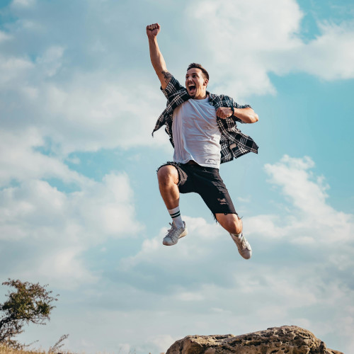 A young man leaping into the air for joy, punching one arm above his head.