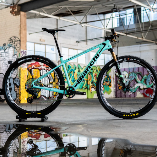 An aqua Bianchi mountain bike, custom-built by Bio-Mechanics Cycles & Repairs. It's photographed in a car park against a colourful graffitied backdrop.