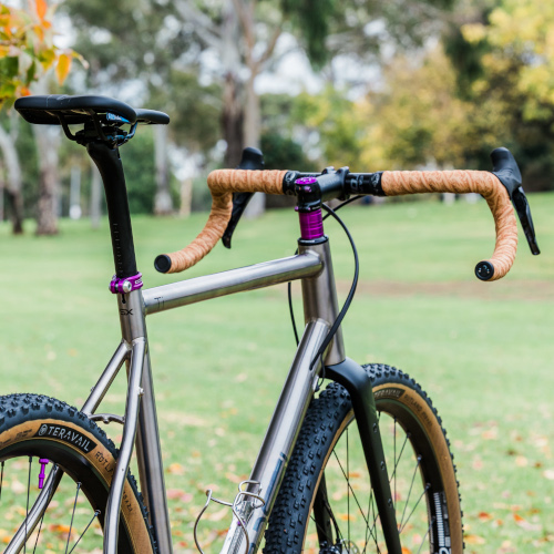 A titanium Bossi Grit gravel bicycle, custom-built by Bio-Mechanics Cycles & Repairs, photographed in a park.