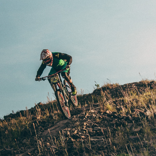 A mountain biker heading downhill on a rocky and grassy slope.