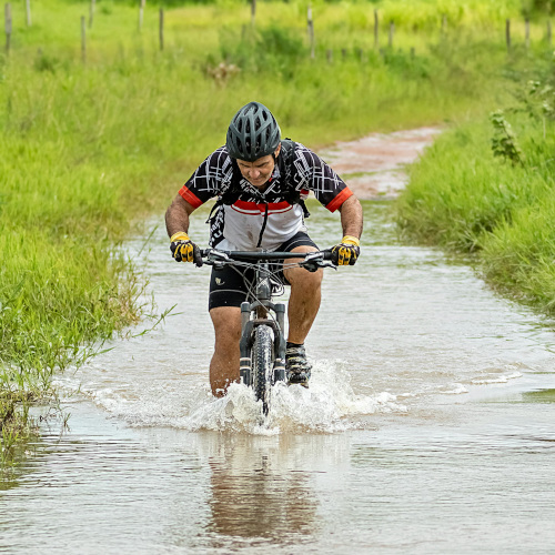 A mountain biker riding through a deep creek, labouring against the water and probably ruining his bike.