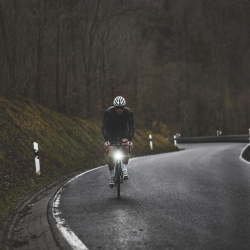 A road cyclist cycling up an incline towards the camera, on a grey and drizzly day.