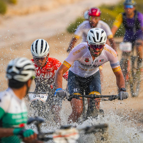 Mountain bikers during a race, crossing a creek or river in a flurry of colour and activity.