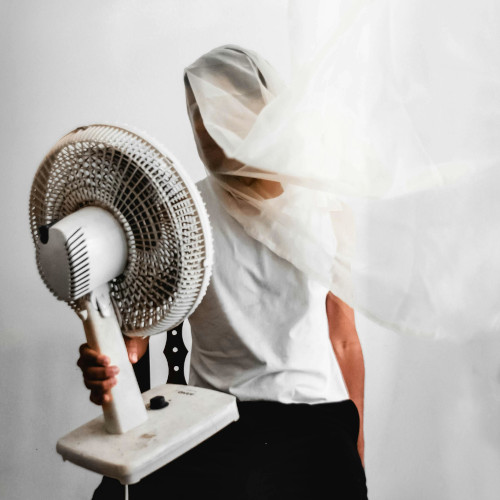 A man with a fan on his lap, aimed at his head, which is wrapped in a piece of gauze.