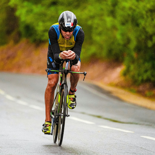 A cyclist riding down a wet road during a race, teeth gritted.