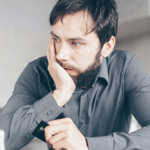 A bearded man holding a credit card, looking traumatised.