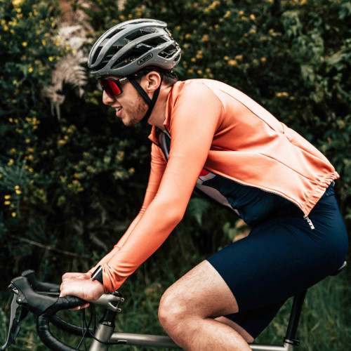 A road cyclist riding, his jersey unzipped and loose.