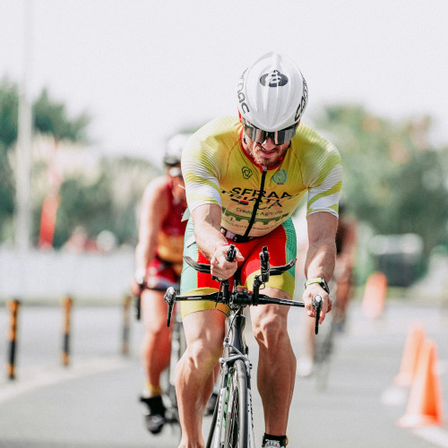 A road or triathlon cyclist during a race, repositioning his hands on his handlebars.