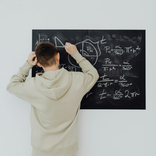 A young man doing complicated maths on a blackboard, scratching his head.