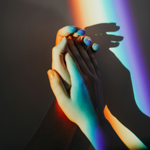 A person clasping their hands in a projection of rainbow light.