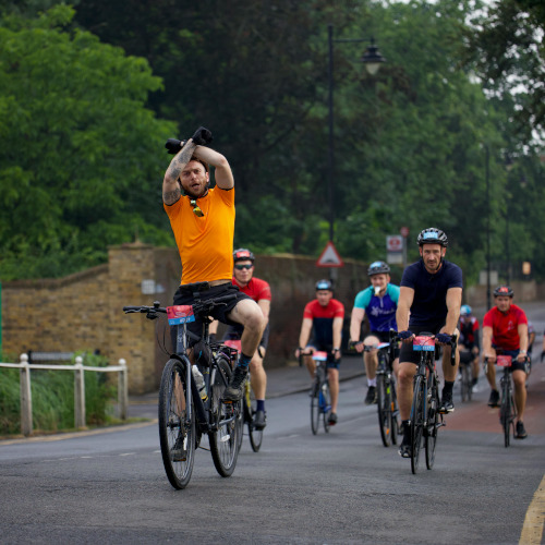 A mountain biker sits up while riding and crosses his arms towards the camera in a victory sign.