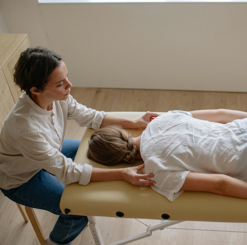 A physical therapist attending to a young woman who is lying face-down on a massage table.