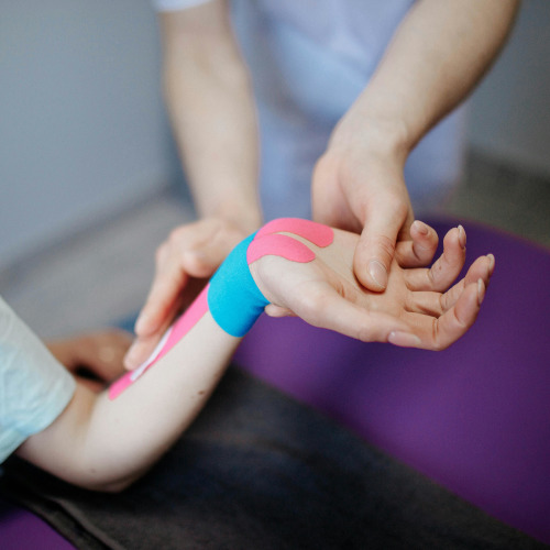 A physiotherapist putting coloured sports tape on a patient's wrist.