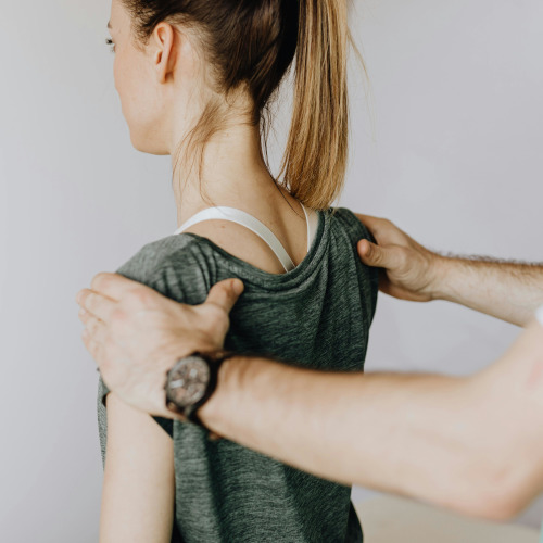 A young woman facing away, a therapist's hands on her shoulders to do a physical assessment.