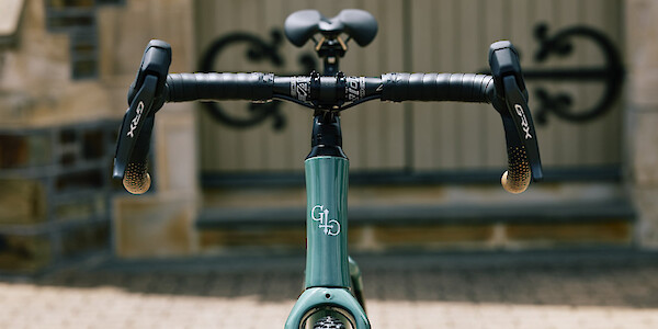 A custom-built Gothic Cycles Aix carbon gravel bicycle in front of a graveyard chapel, showing headtube badge detail