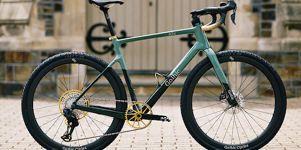 Custom-build Gothic Cycles Aix carbon gravel bike, in shades of green and gold, in front of a graveyard chapel.