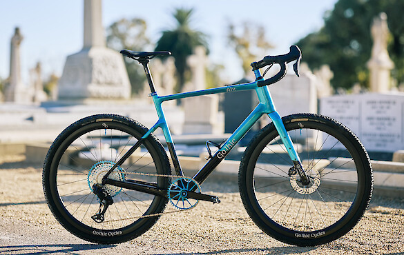 Custom-built carbon gravel bike by Gothic Cycles in a blue and black colour scheme, photographed in a graveyard
