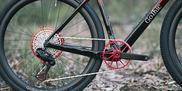 Red and black Garbaruk drivetrain components on a custom-built Gothic Cycles carbon gravel bike, photographed in a forest
