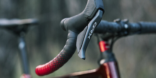 Shimano GRX levers and red and black Ciclovation bar tape on a custom-built Gothic Cycles carbon gravel bike, photographed in a forest